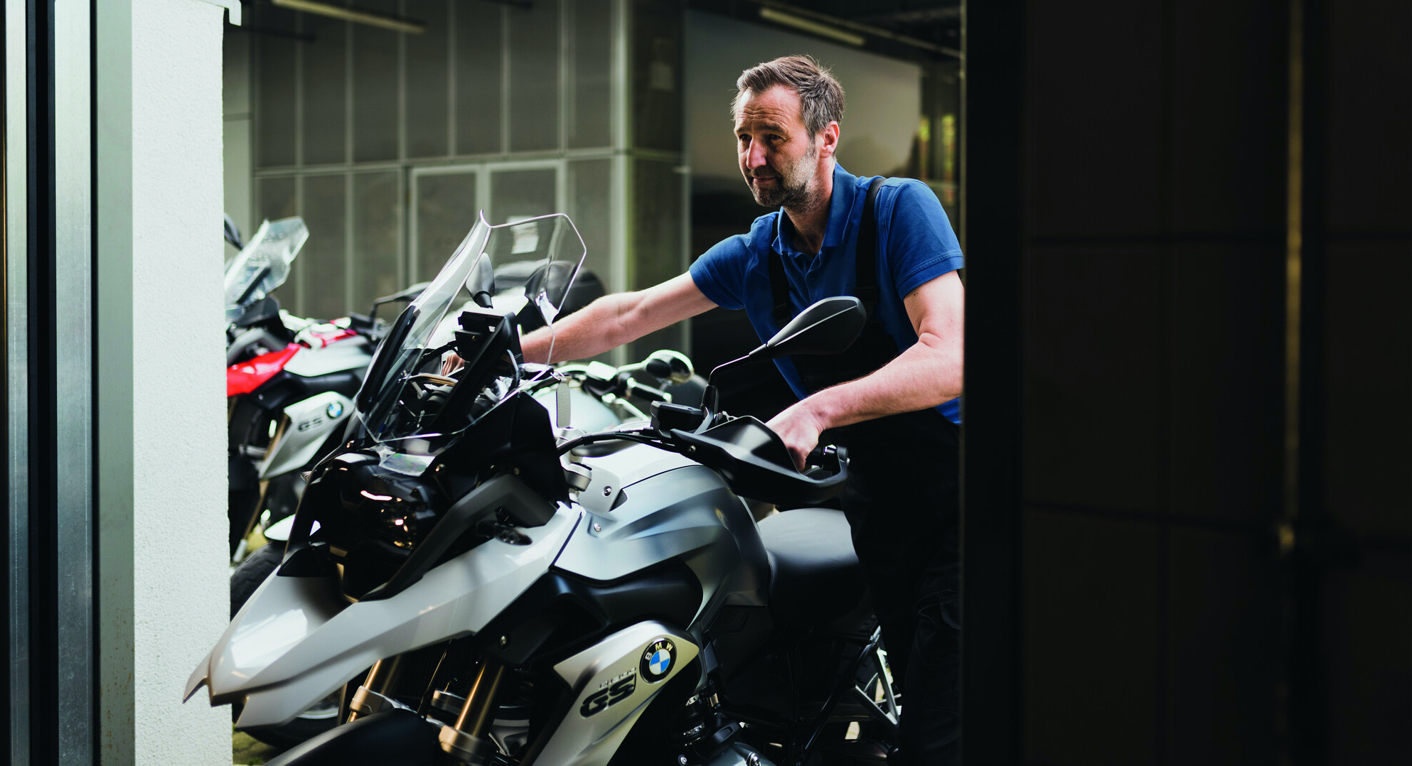 Mekaniker trækker hvid BMW GS motorcykel ind gennem port