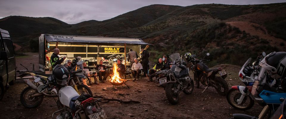 Offroad motorcykler og cyklister omkring bål om aftenen i bjergrigt landskab