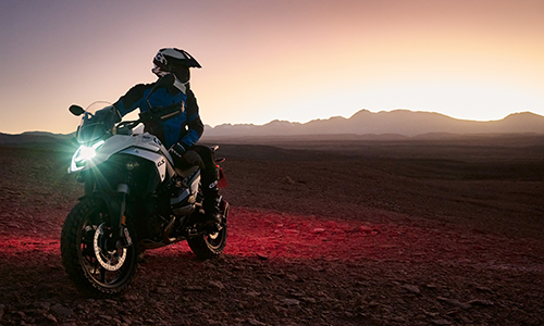 Mand holder i stenet bjerglandskab på hvid BMW motorcykel og kigger sig tilbage