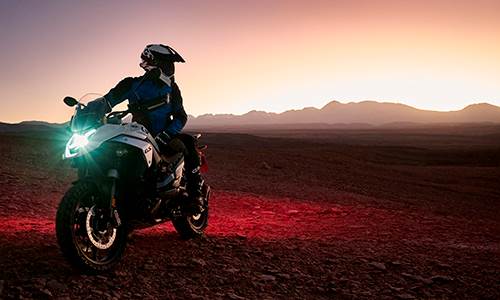 Mand holder i stenet bjerglandskab på hvid BMW motorcykel og kigger sig tilbage