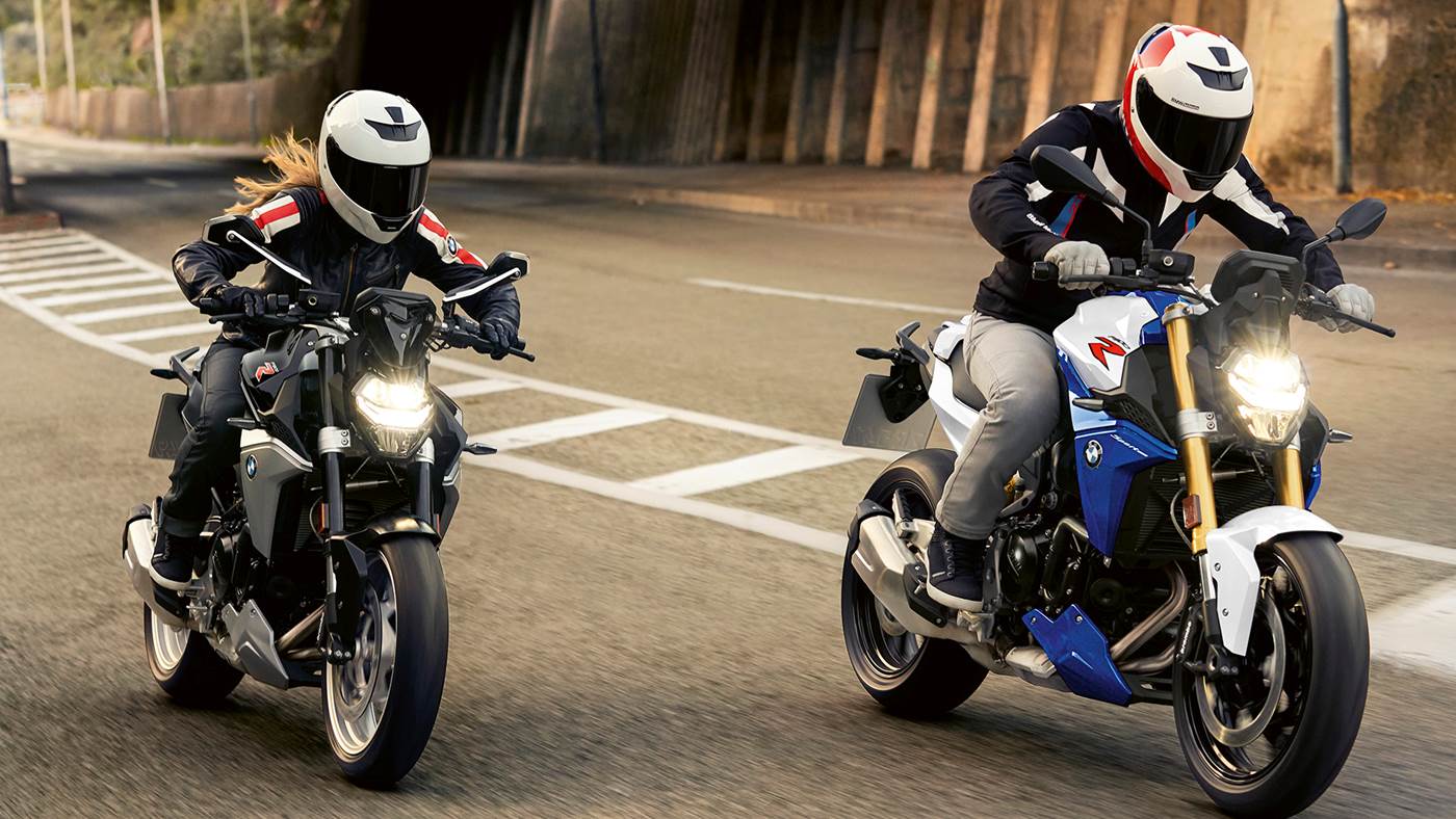 To personer kører motorcykel på vej i bymiljø