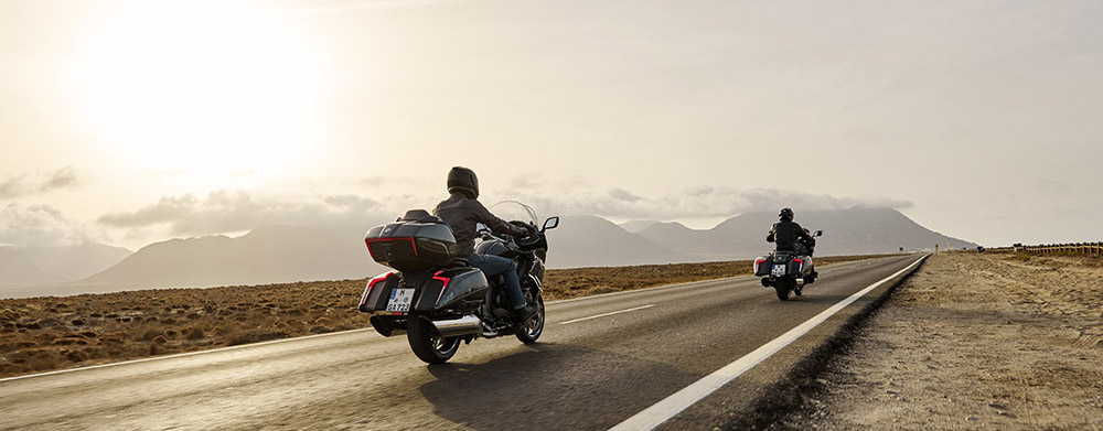 To store BMW motorcykler kører væk på lang lige vej i bjerglandskab